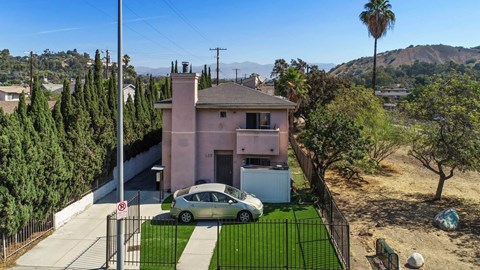 A car is parked in front of a pink house with a black fence.
