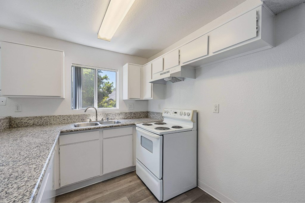 A white kitchen with a stove, sink, and cabinets.