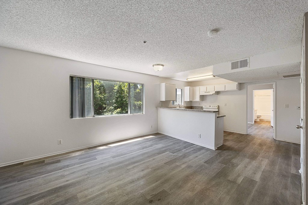 A spacious kitchen and living room with wood flooring and white walls.