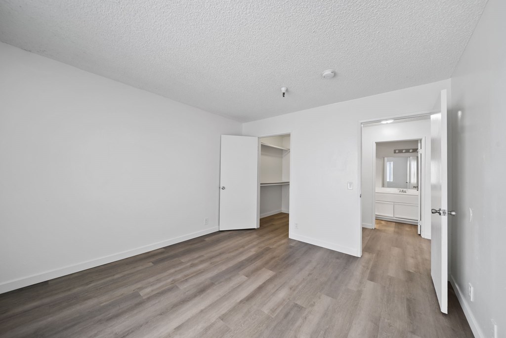 A room with white walls and wood flooring with a doorway leading to another room.