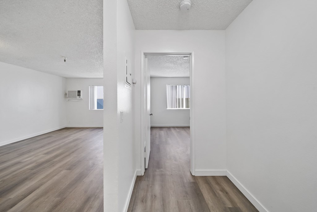 A long, narrow, empty room with wood floors and white walls.