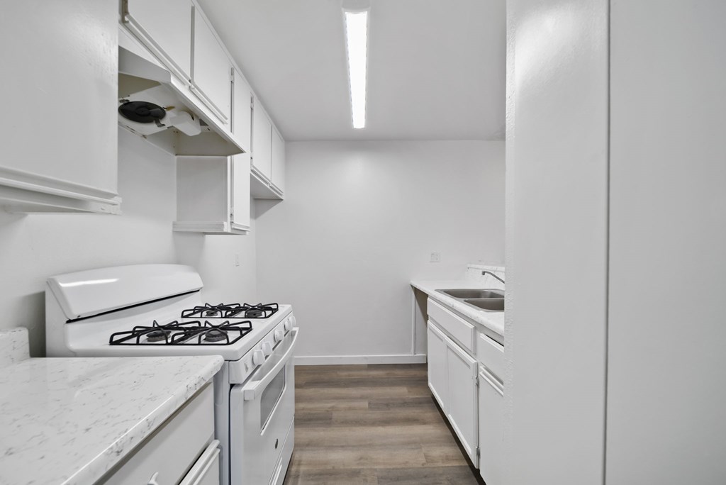 A white kitchen with a stove, sink, and cabinets.