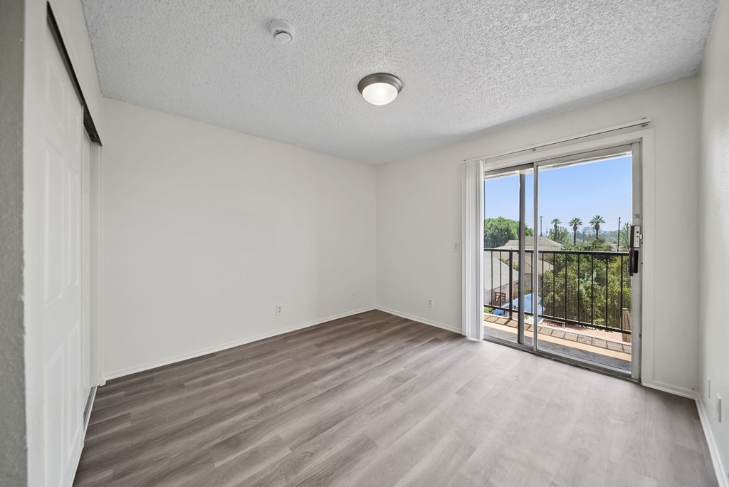 A room with a sliding glass door leading to a balcony with a view of a fence and trees.