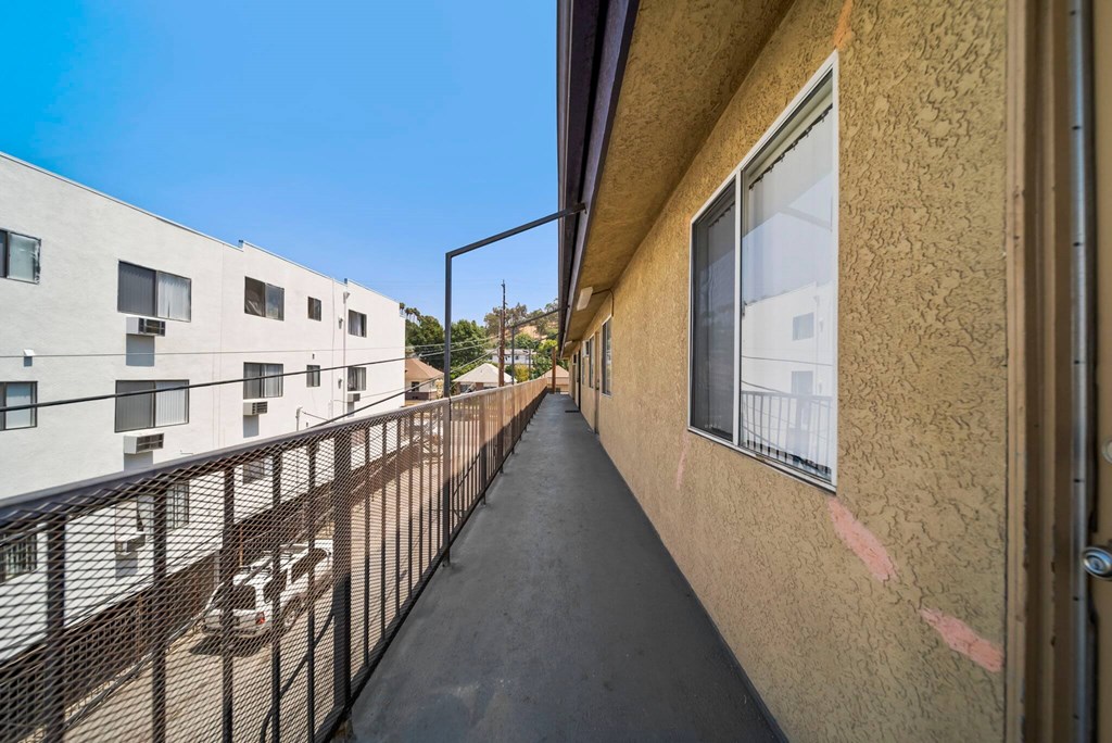 A long balcony with a black railing and a tan wall.
