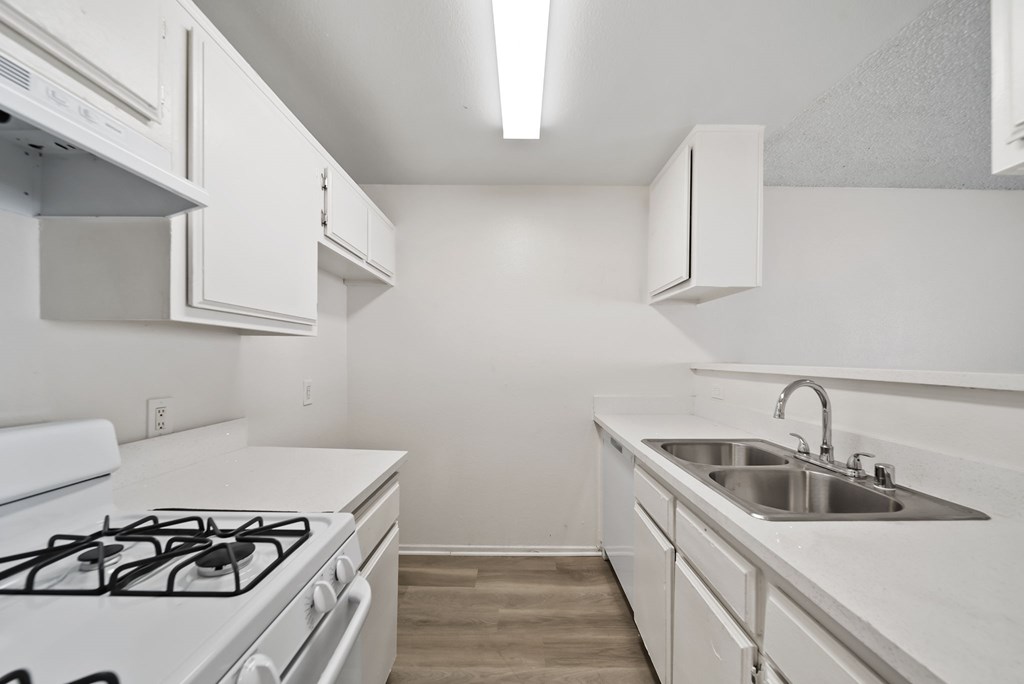 A white kitchen with a stove, sink, and cabinets.