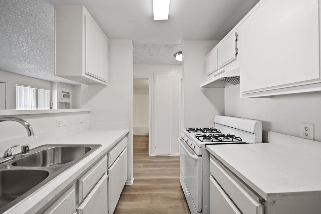 A white kitchen with a stove, sink, and cabinets.
