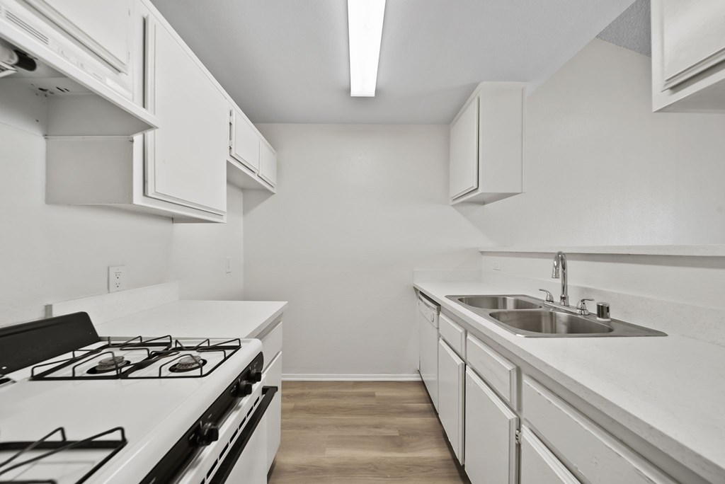 A white kitchen with a stove, sink, and cabinets.