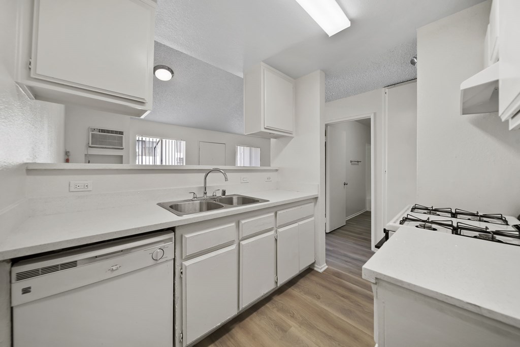 A white kitchen with a stove, sink, and cabinets.