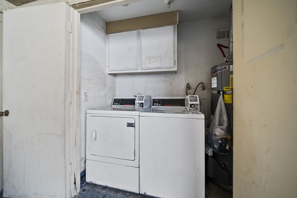 A white washing machine and dryer in a small, dirty laundry room.