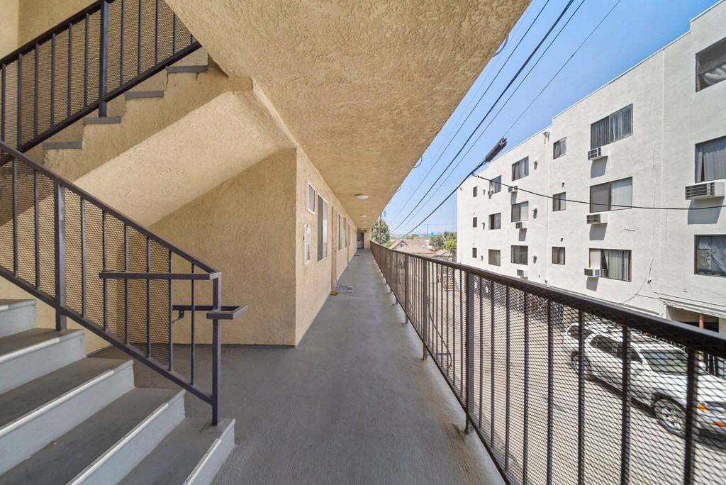 A long, narrow hallway with a metal railing and steps leading up to a building.