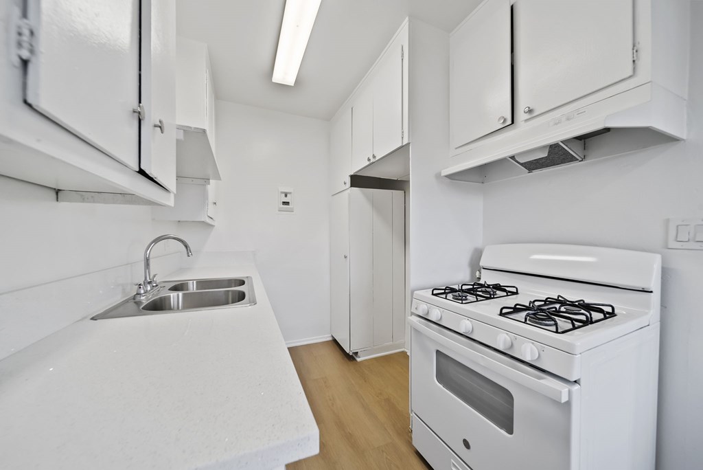 A white kitchen with a stove, sink, and cabinets.