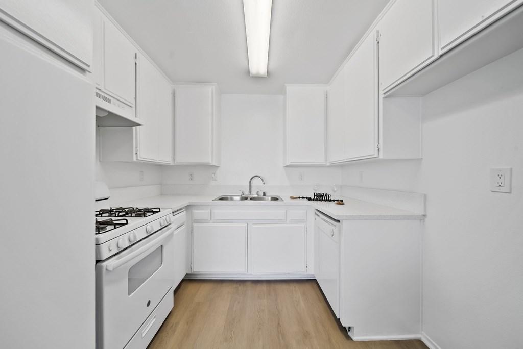 A white kitchen with wooden floors and white appliances.