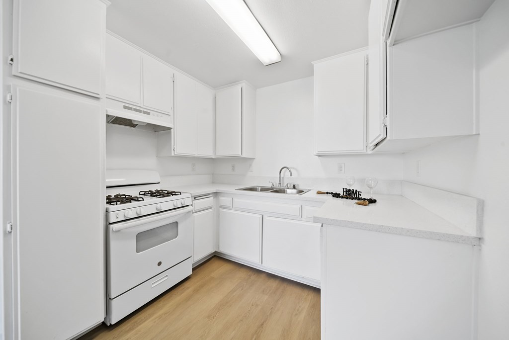 A white kitchen with a stove, sink, and cabinets.