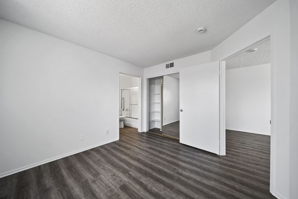 A room with white walls and wood flooring with a doorway leading to another room.