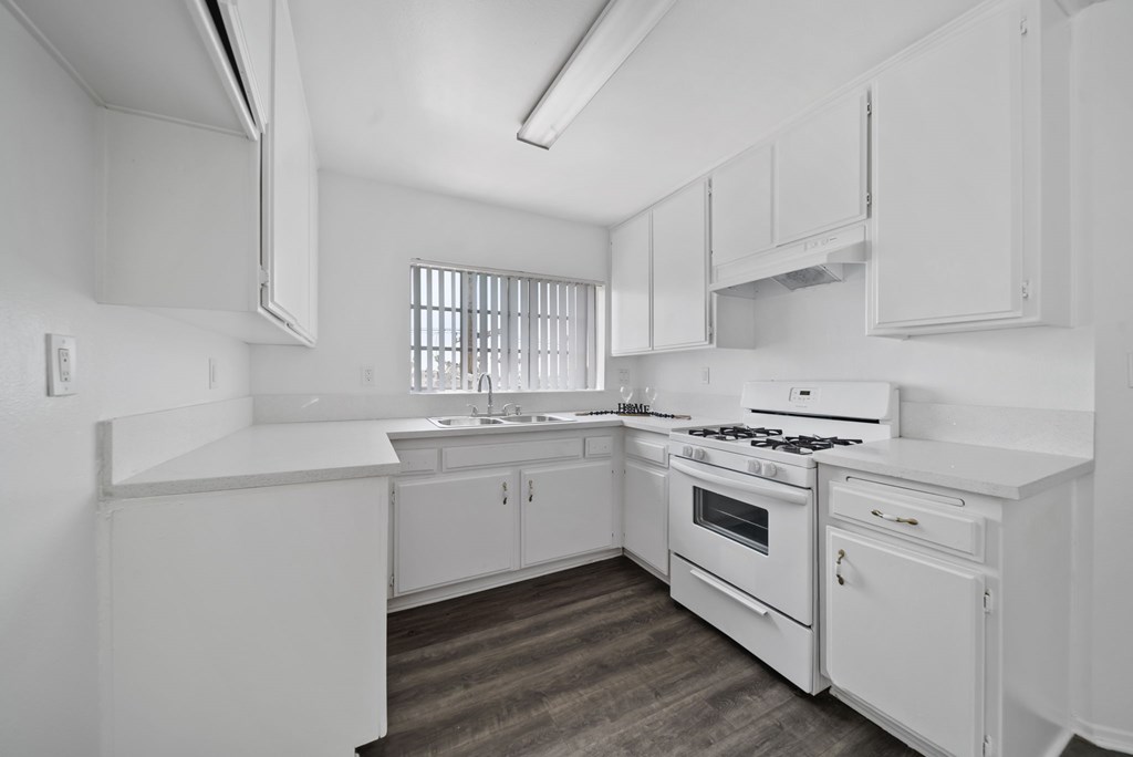 A white kitchen with a stove, sink, and cabinets.