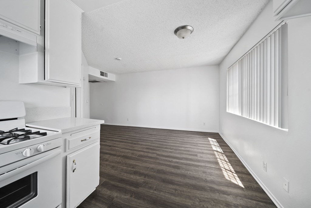 A kitchen with a stove, cabinets, and a window with blinds.