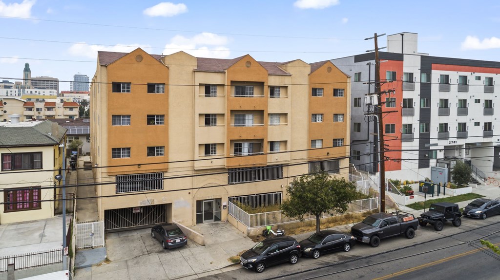 A street view of a multi-story building with cars parked in front.