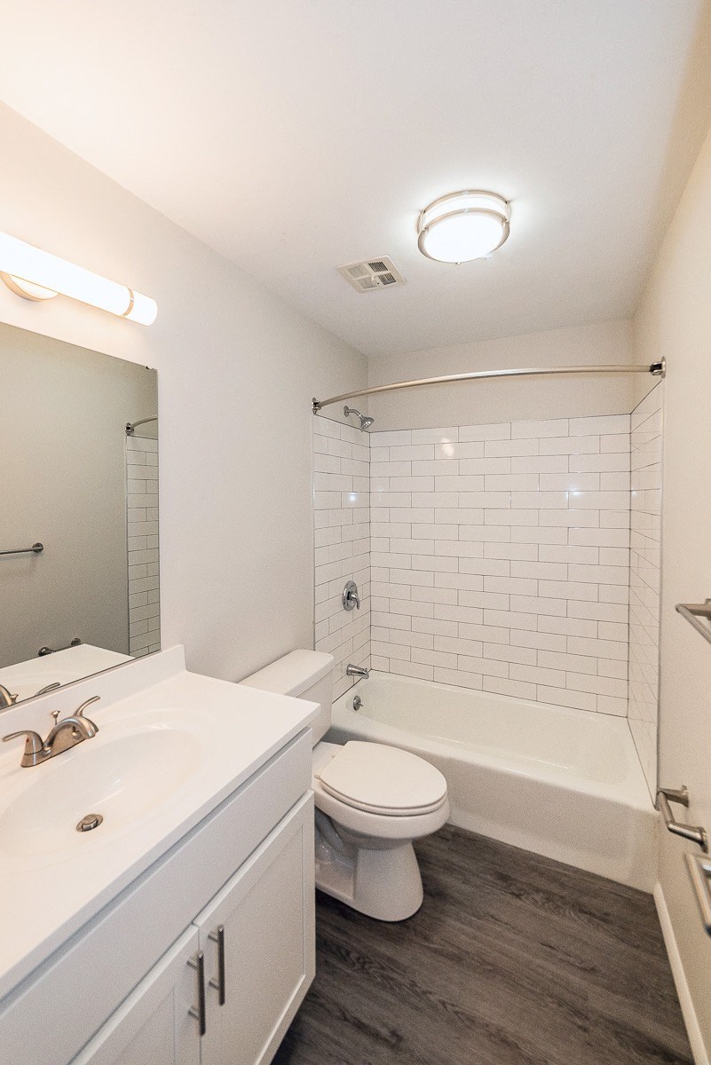 Fully renovated bathroom with subway tile, gray plank flooring, and white vanity at Kings Gate West Apartments, Camillus, NY, 13031