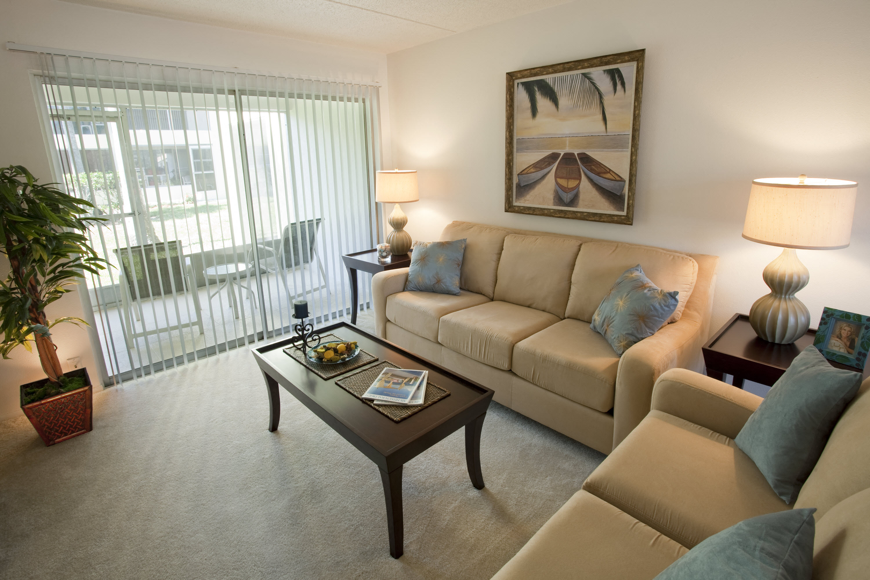 A living room with a tan couch, a coffee table, and a painting on the wall.