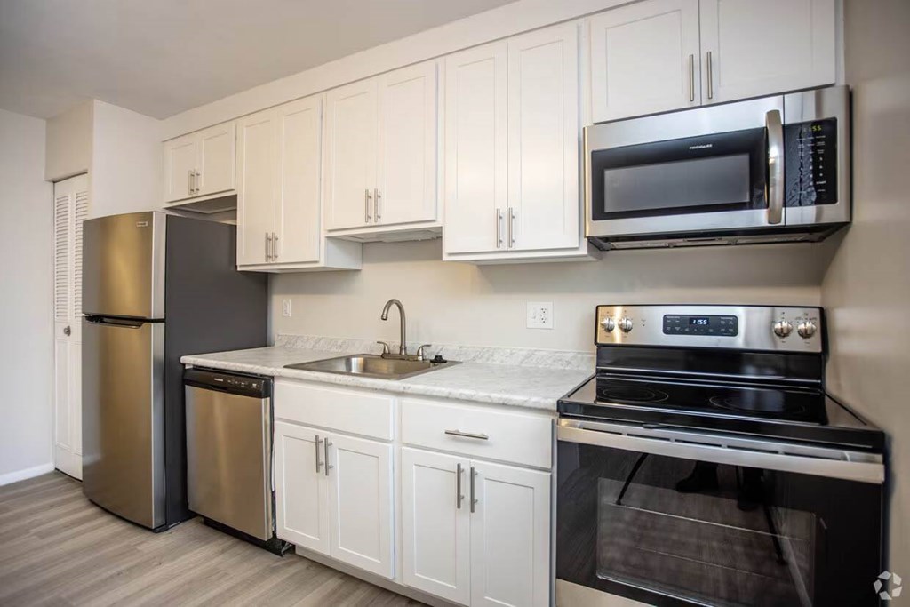 A kitchen with white cabinets and black appliances at Kings Gate West Apartments, Camillus, New York