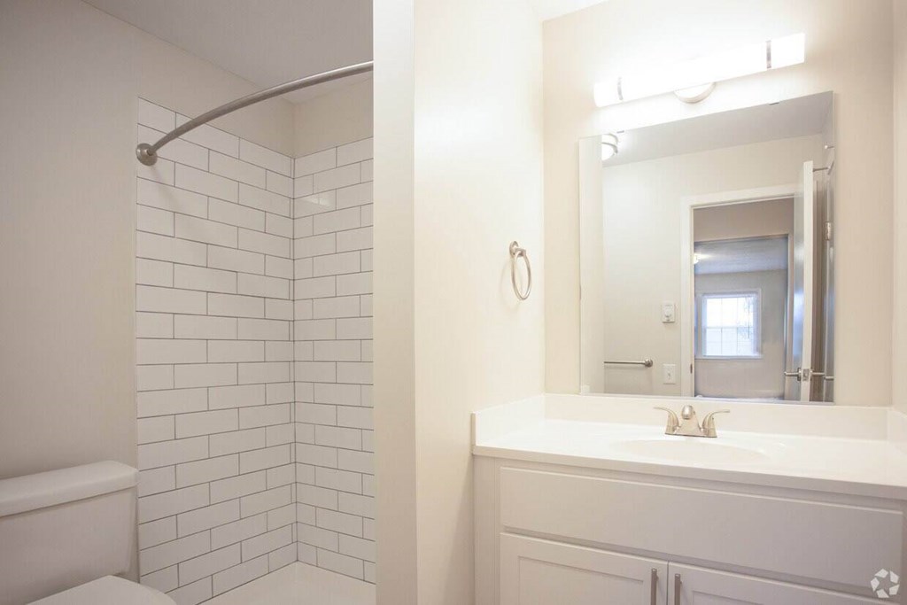 A white bathroom with a white toilet, a white sink, and a white tiled shower at Kings Gate West Apartments, New York