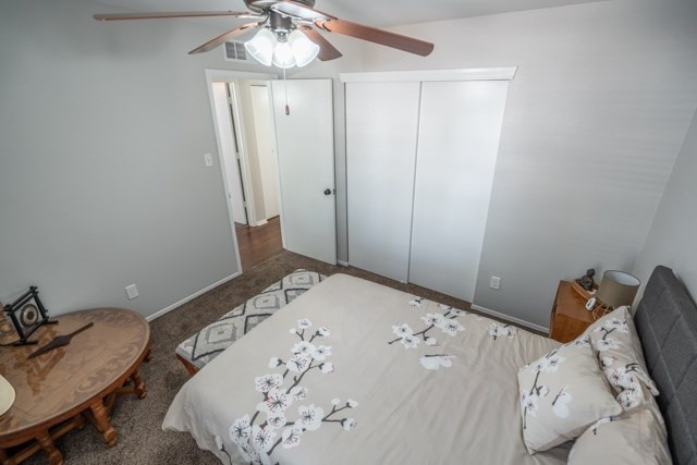 A bedroom with a bed, a ceiling fan, and a small table.