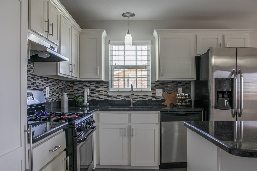 a kitchen with white cabinets and black countertops and splash guards at Village of Cottonwood Springs