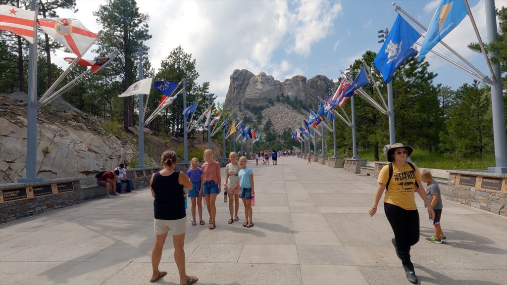 a group of people walking on a bridge with flags and mountains in the background  at Antelope Ridge, Box Elder, SD