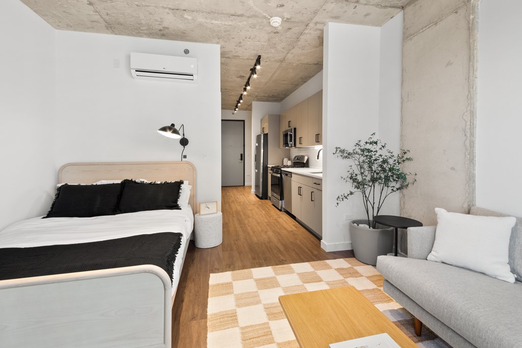 A bedroom with a bed, a couch, and a small kitchen area.