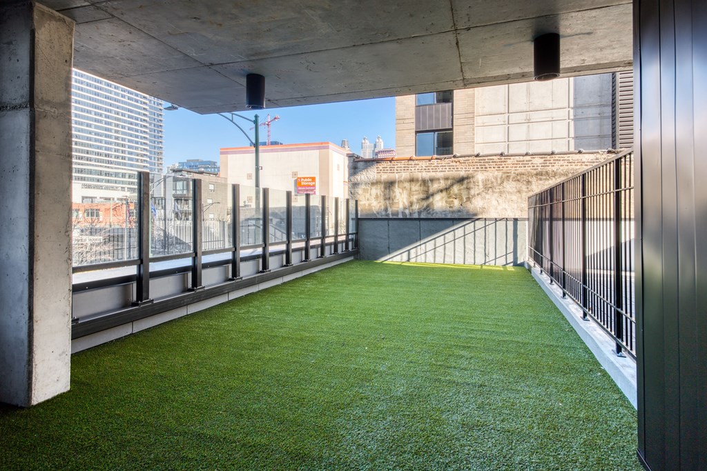 A green lawn is surrounded by a metal fence and concrete pillars.