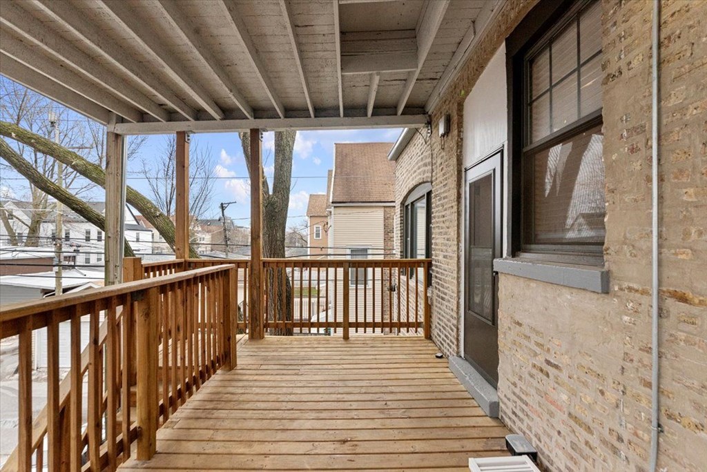 A wooden deck with a railing and a brick building in the background.
