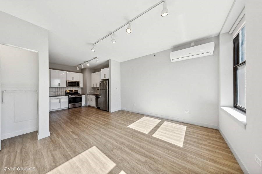 an empty living room with a kitchen in the background