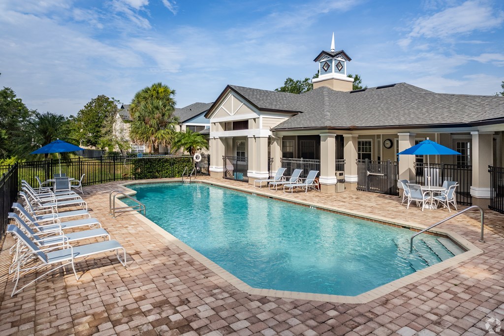 A pool surrounded by chairs and umbrellas in front of a house.