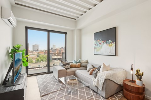 A living room with a grey couch and a large window overlooking the city.