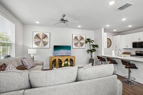 A living room with a grey couch, a fan, and a painting on the wall.