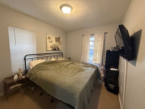 A bedroom with a bed, nightstand, and window with blinds.