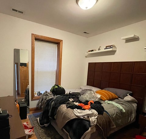 A bedroom with a messy bed and a window with blinds.