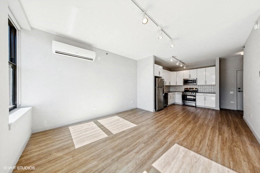 an empty living room with a kitchen in the background