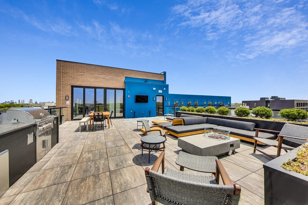 a rooftop patio with a barbecue grill and a blue building in the background