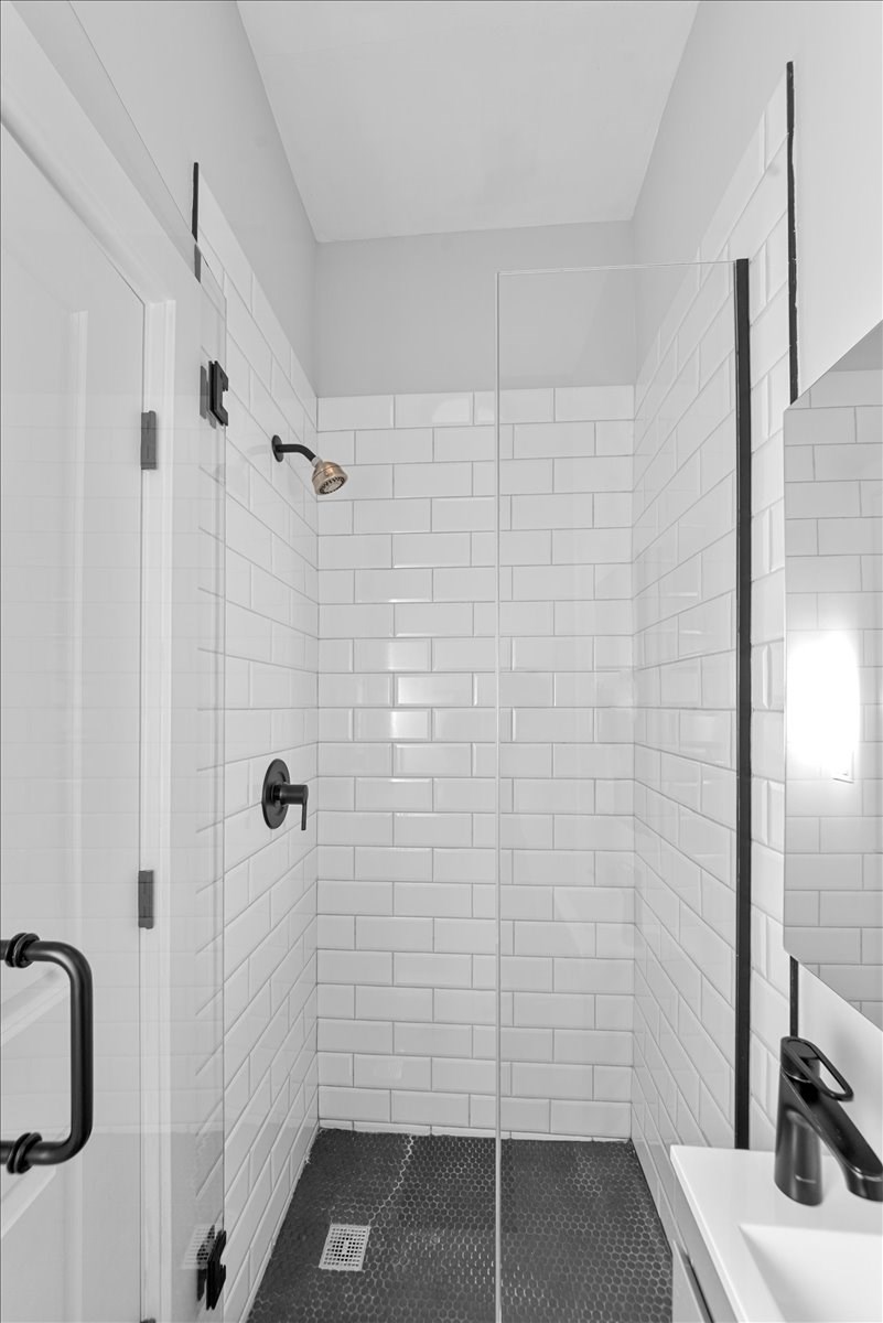 A white tiled bathroom with a black shower head and a black and white shower curtain.