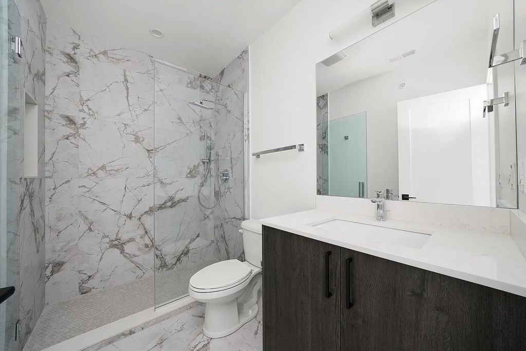 A white toilet sits in a bathroom with a marble wall.