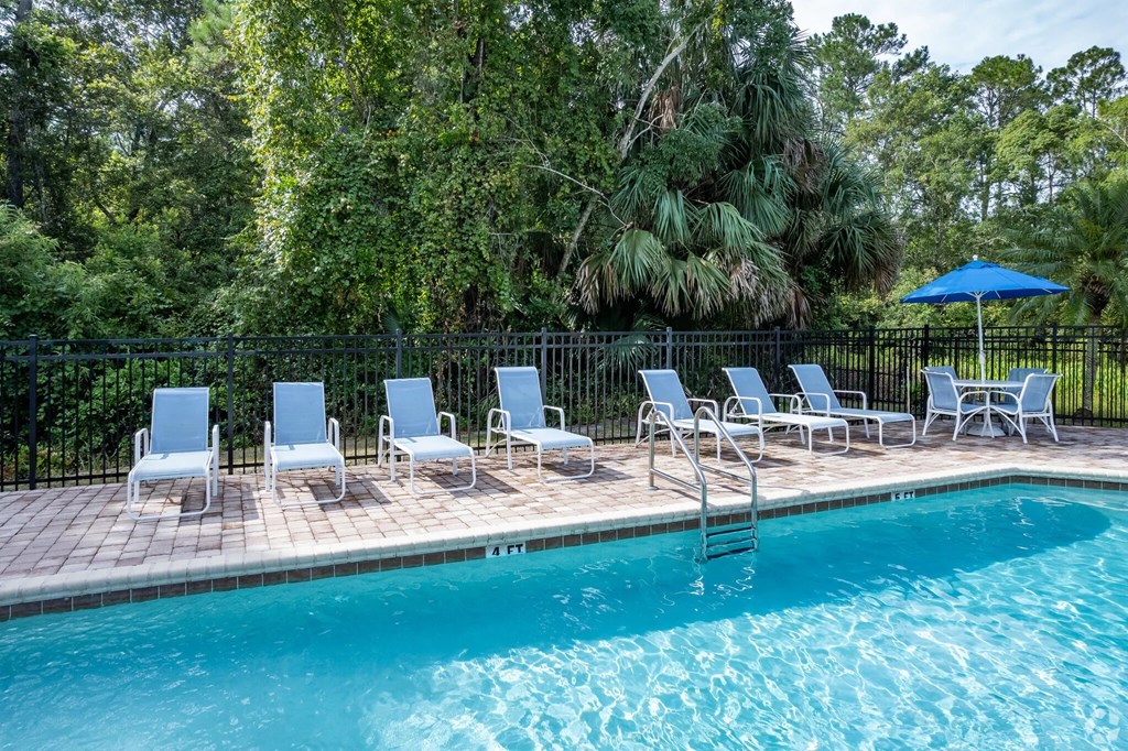 A pool surrounded by trees and chairs.