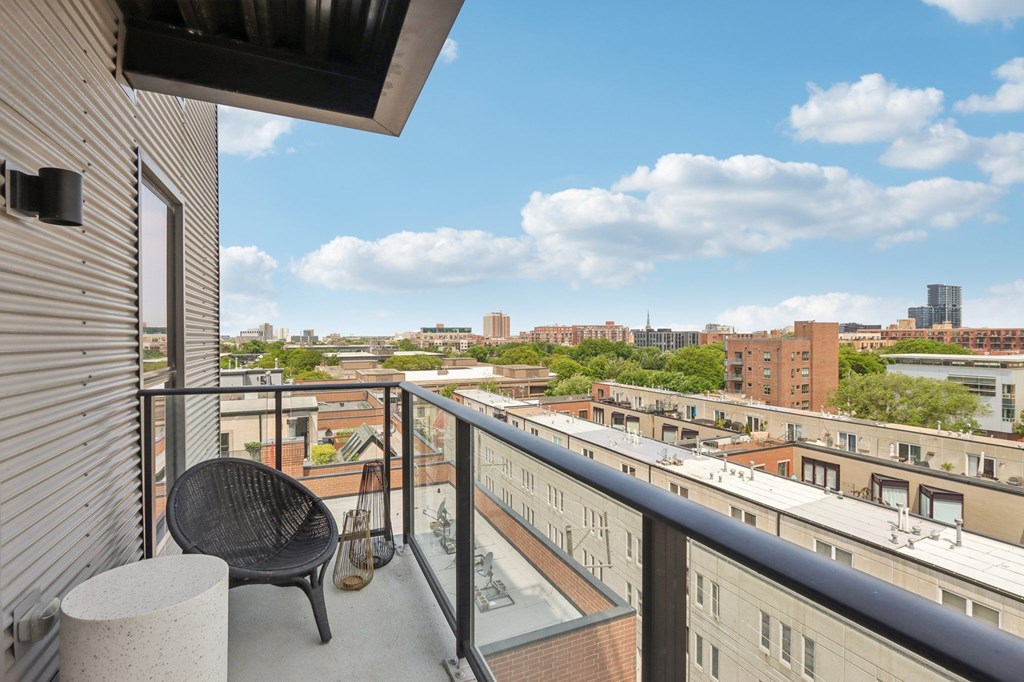 A balcony with a chair and table overlooks a cityscape.
