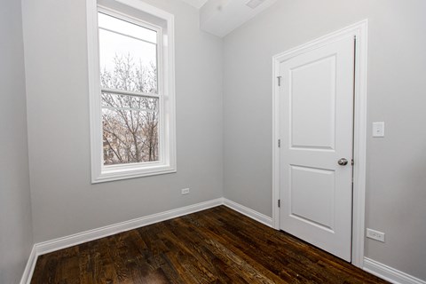 A room with a white door and a window with a view of trees.