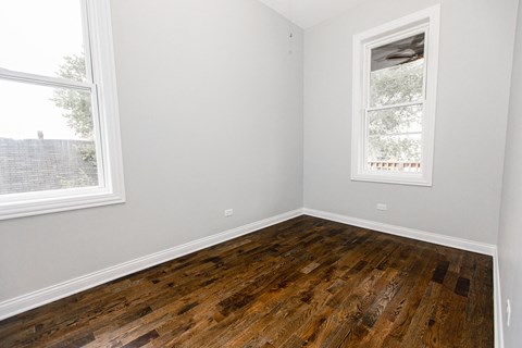 an empty room with wooden floors and two windows