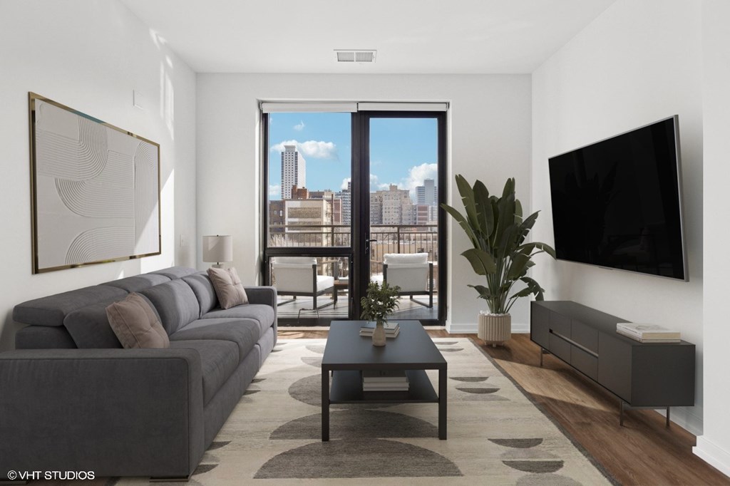 A modern living room with a grey couch, a coffee table, a flat screen TV, and a large window with a view of the city.