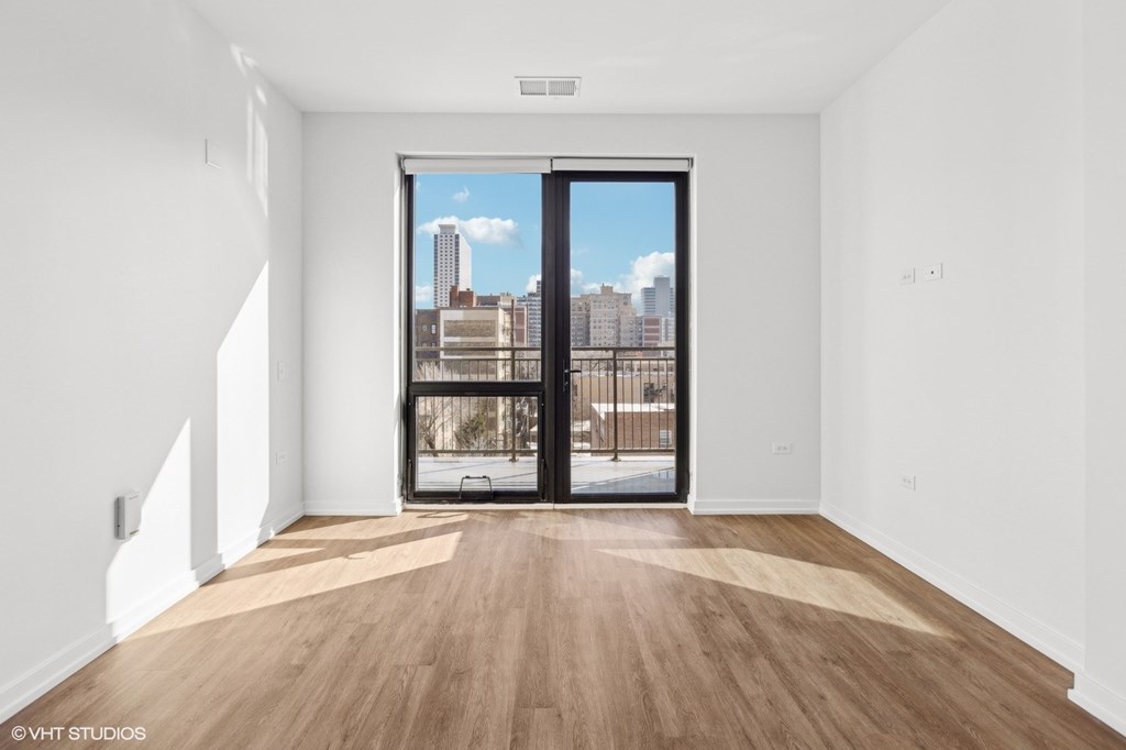 A room with a wooden floor and a view of the city through a glass door.