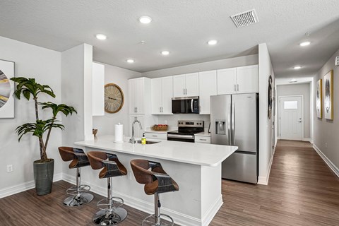 A kitchen with white cabinets and a white island with brown bar stools.