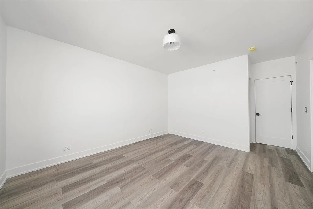 A room with a wooden floor and a smoke detector on the ceiling.