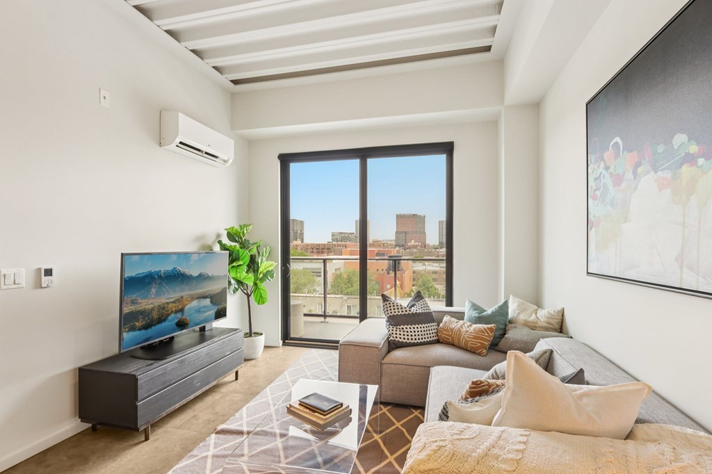 A living room with a large window, a flat screen TV, a couch, and a rug.